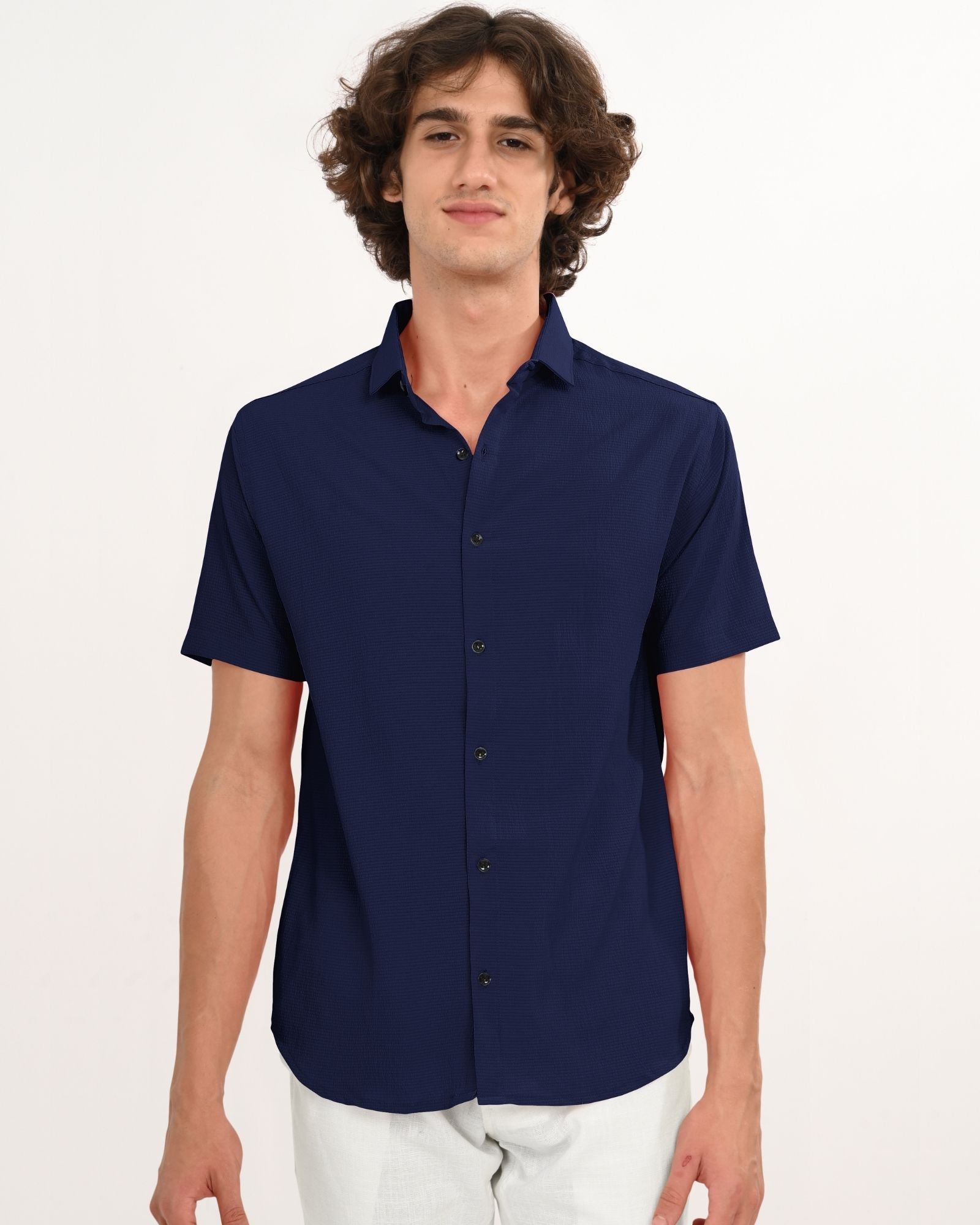 Front view of navy textured short-sleeve shirt styled with white pants