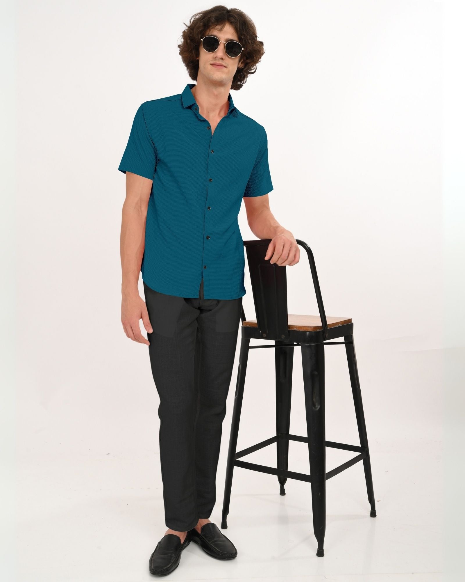Full body shot of man in teal short sleeve shirt paired with black trousers and loafers