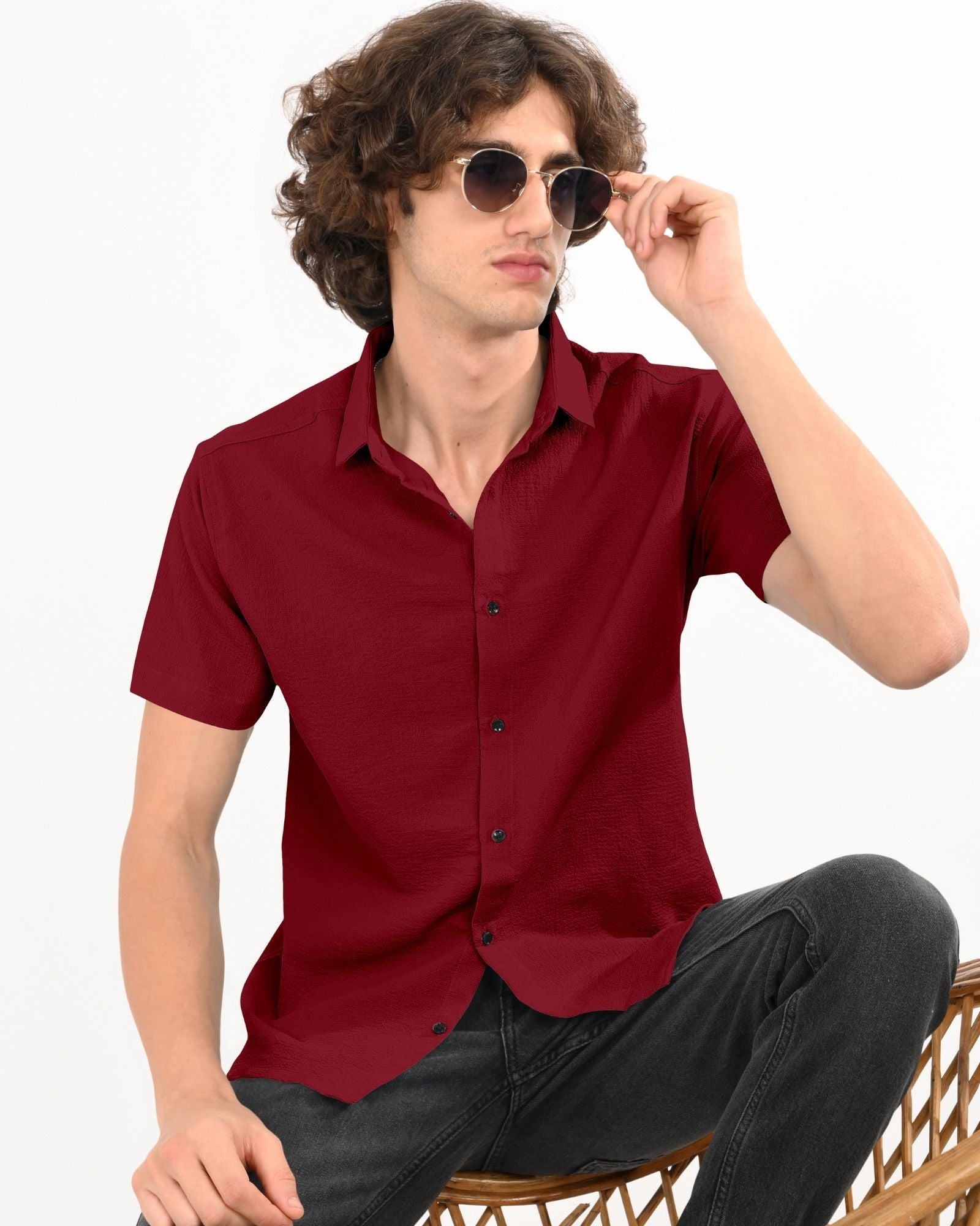 Man adjusting sunglasses while wearing a crimson red short sleeve textured shirt with black buttons.