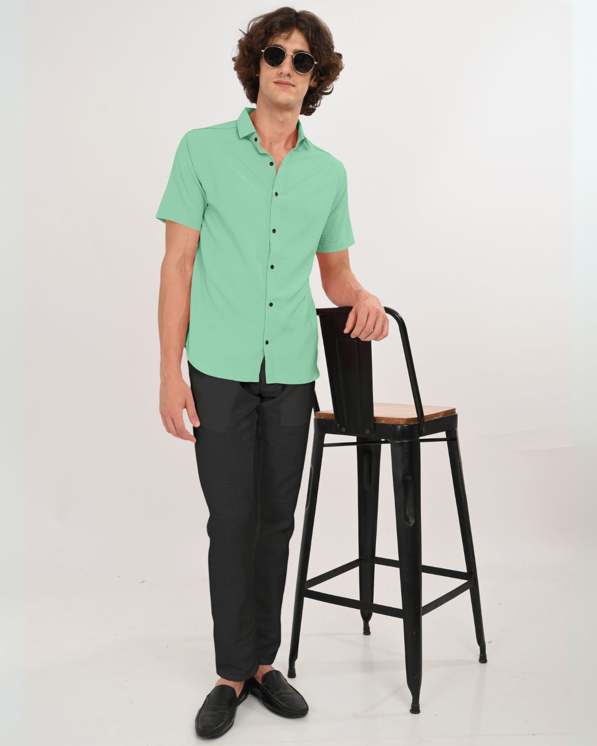 Man in mint green short sleeve shirt standing by chair