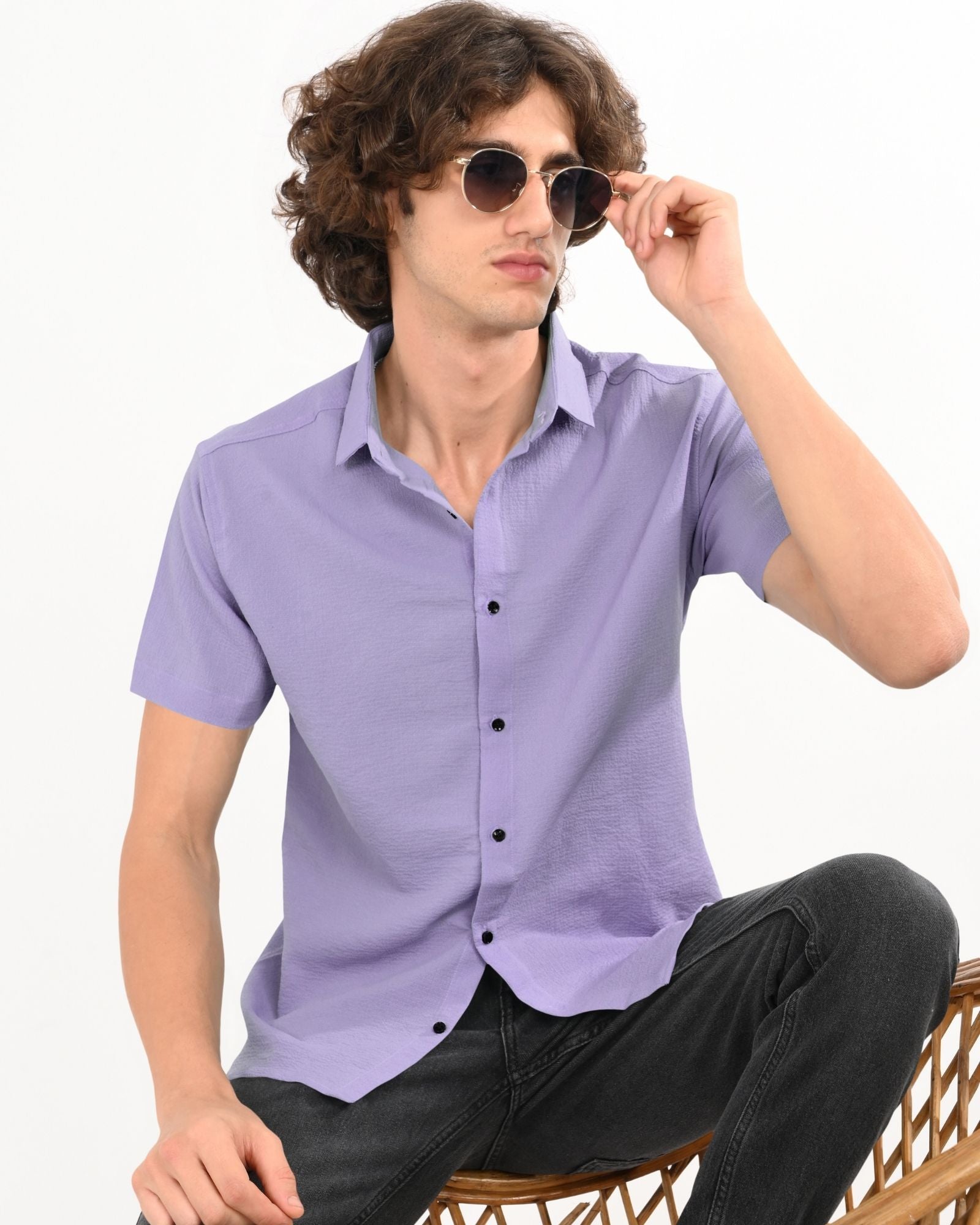 Model sitting on a chair wearing lavender short-sleeve textured button-up shirt with black buttons