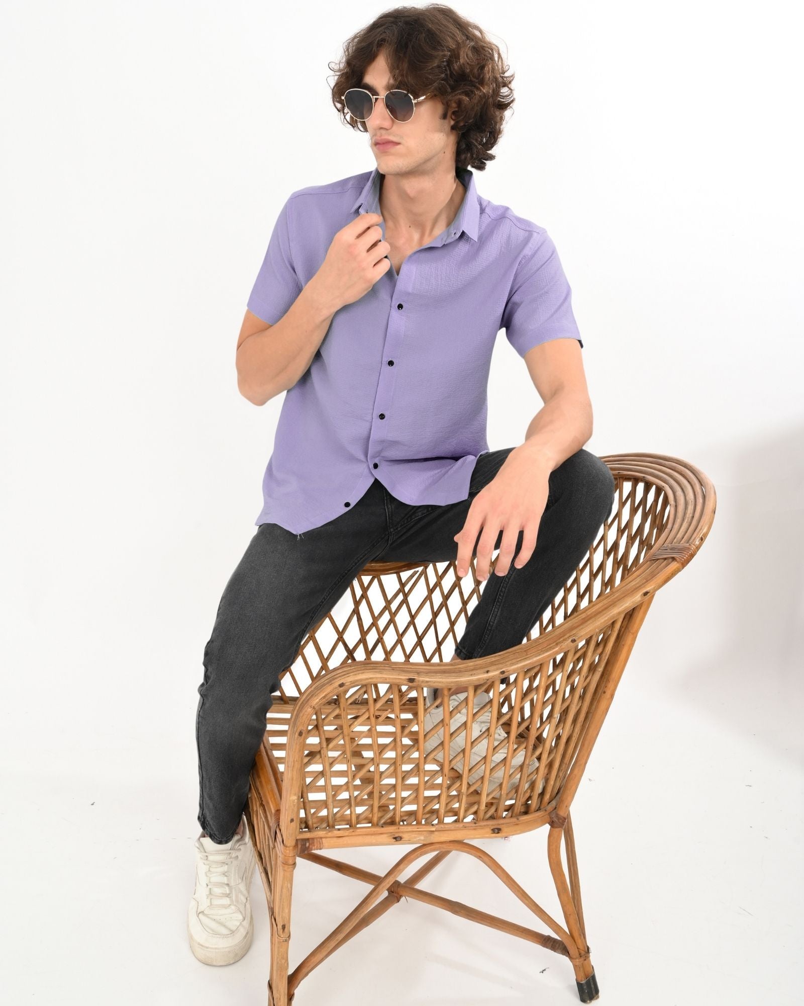 Model sitting on wicker chair wearing lavender button-up short-sleeve shirt with casual style