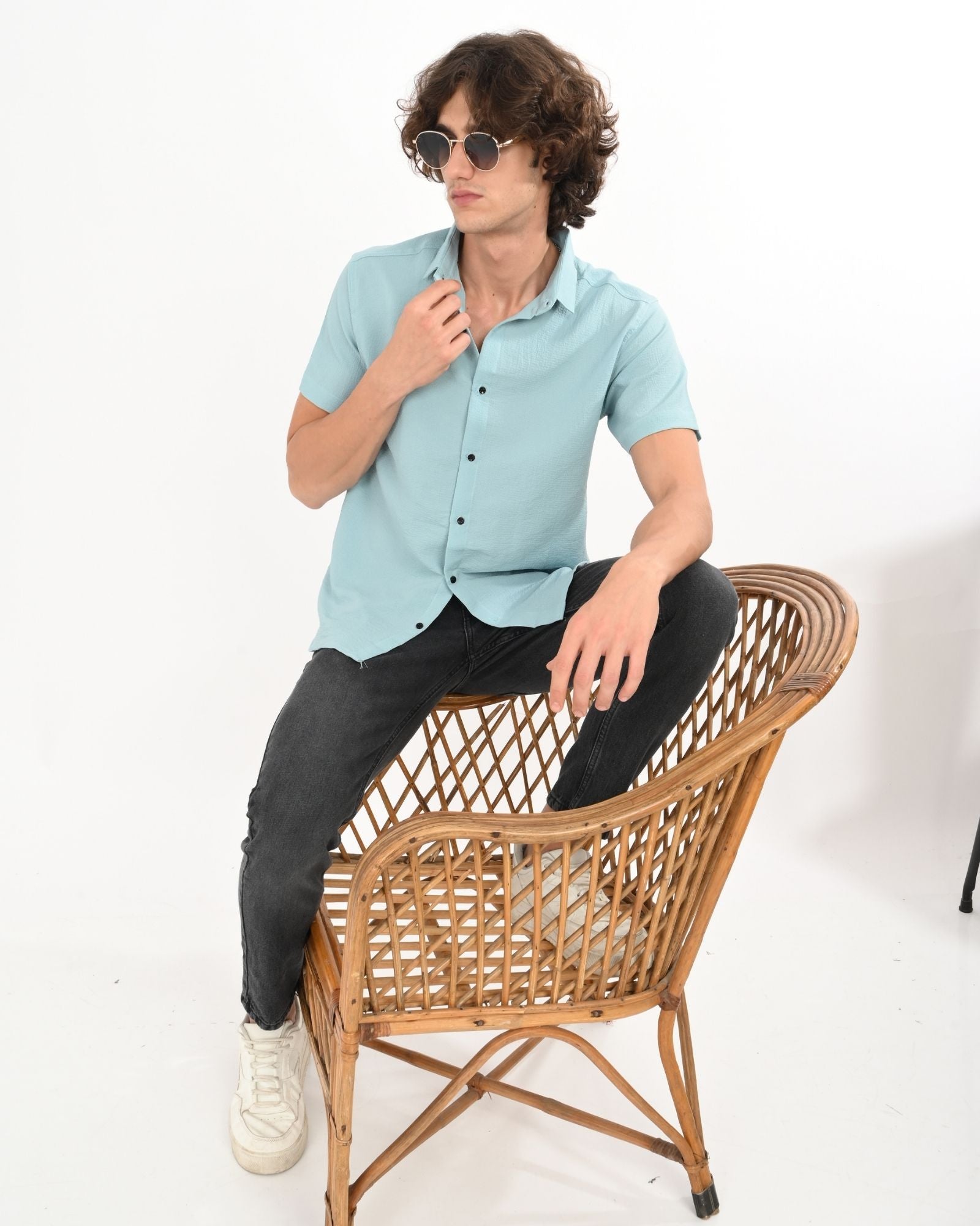 Full body view of man in light blue textured short sleeve shirt and black jeans, casual look