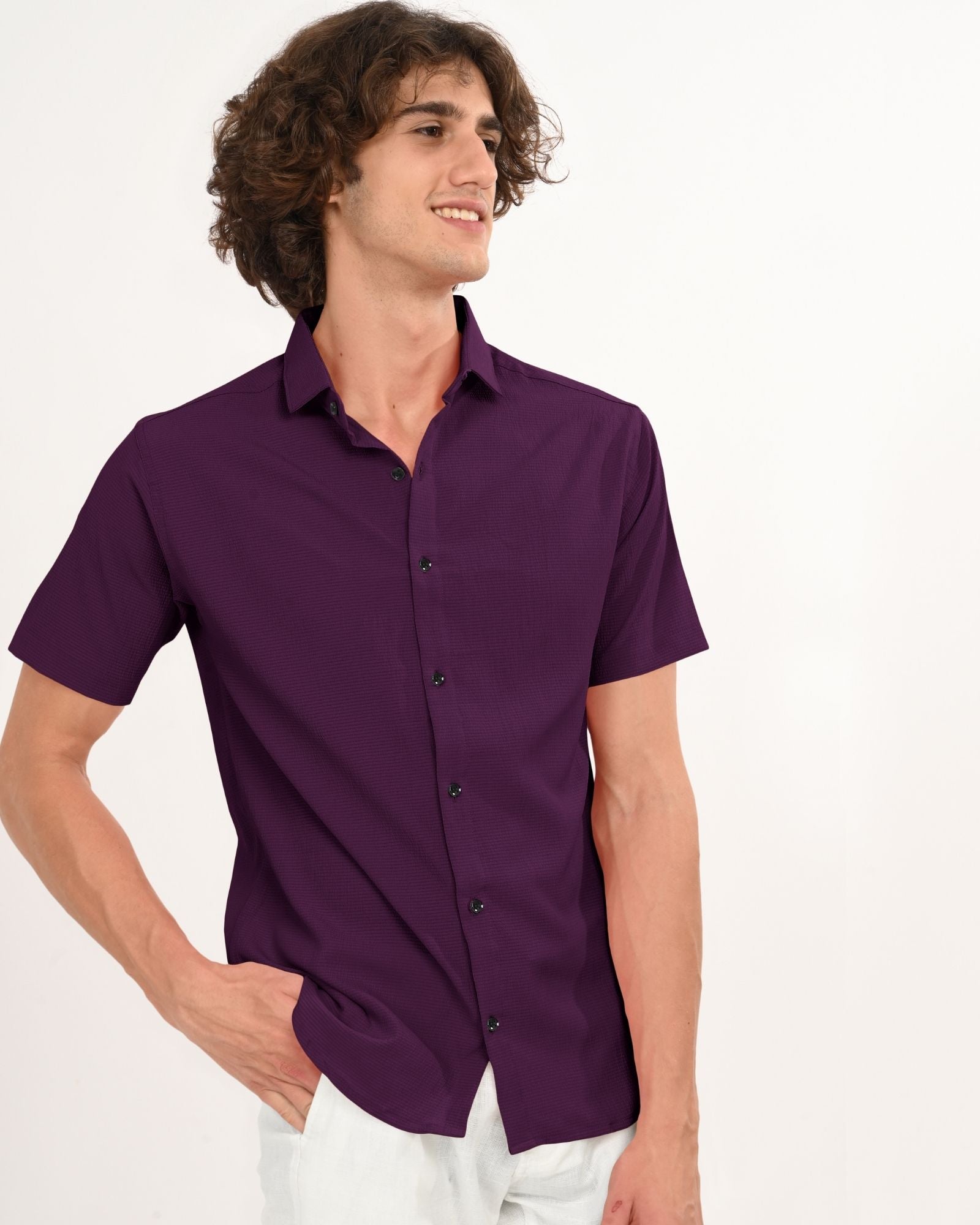 Man in a royal plum short sleeve button-down shirt looking sideways with one hand in pocket