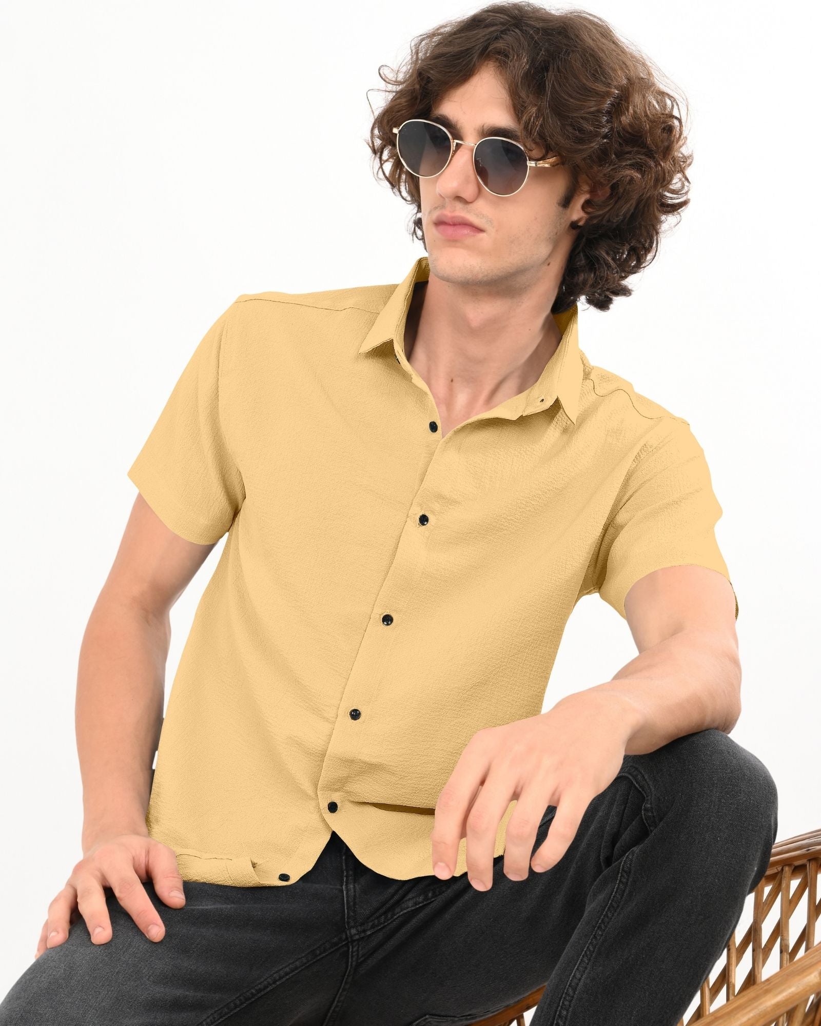 Man in beige textured casual short sleeve shirt and black jeans, seated on a chair