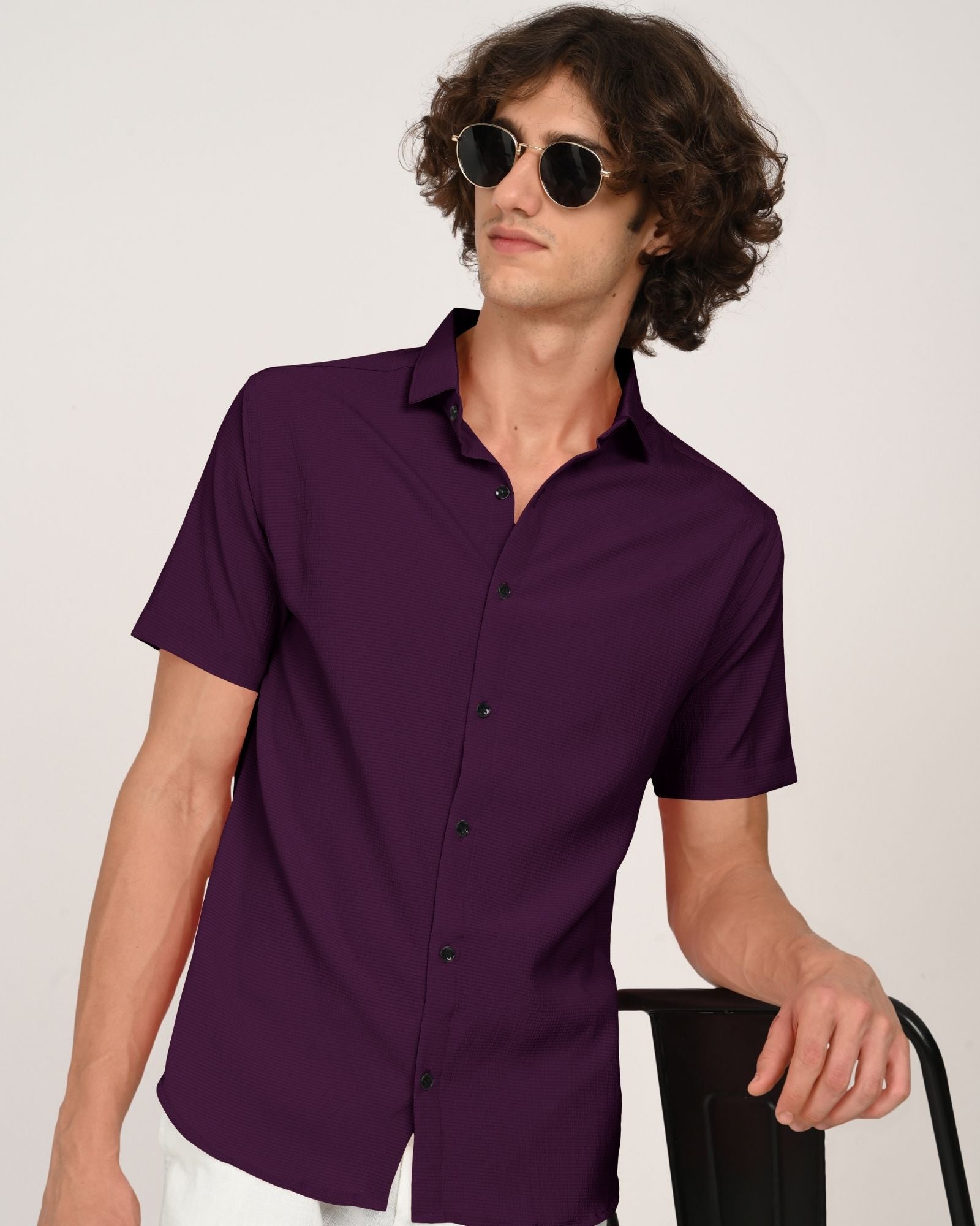 Man in royal plum short sleeve button-down shirt and sunglasses leaning on a chair