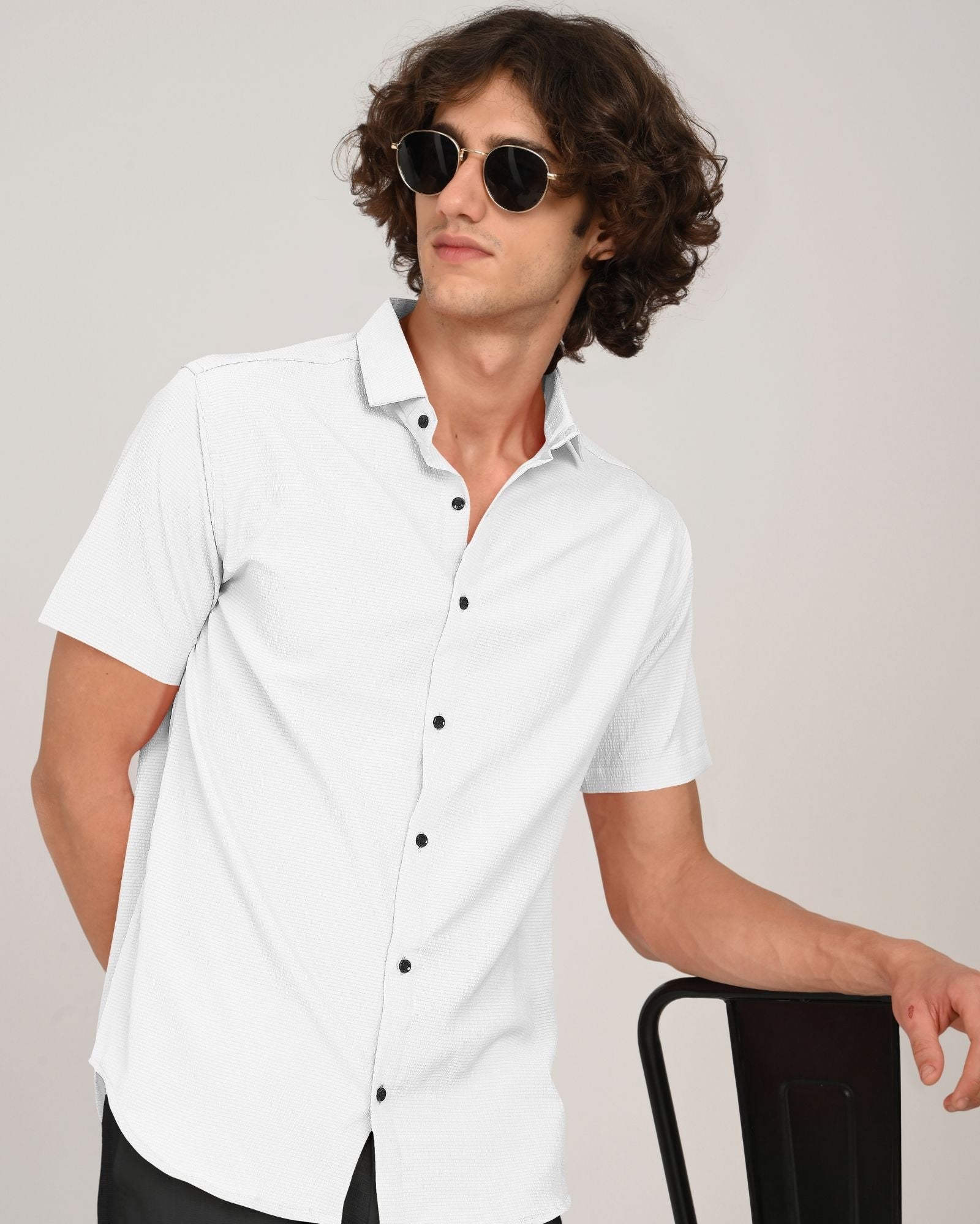 Man in sunglasses wearing white short sleeve button-down shirt leaning on chair