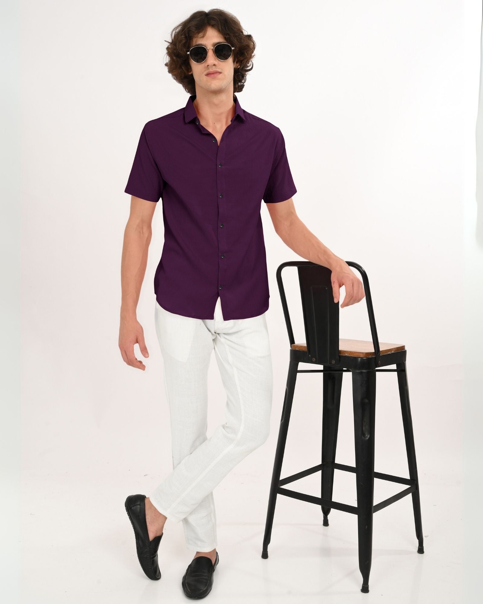 Man wearing a royal plum short sleeve button-down shirt with white trousers and sunglasses