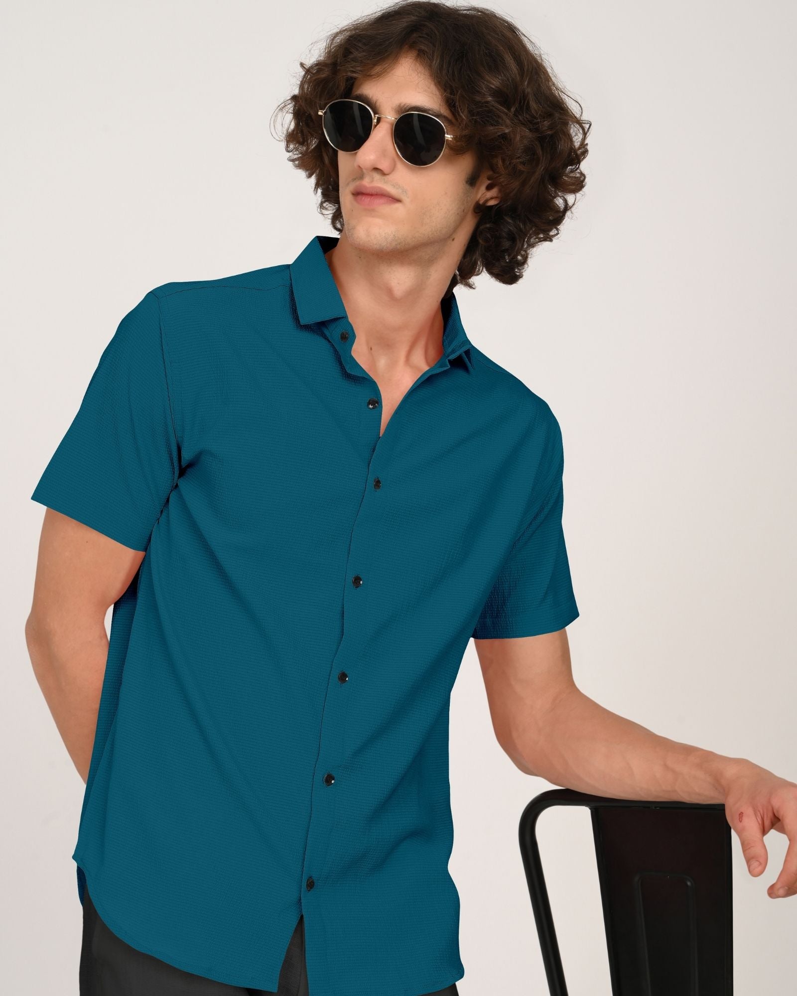 Man wearing sunglasses and teal short sleeve shirt leaning on chair