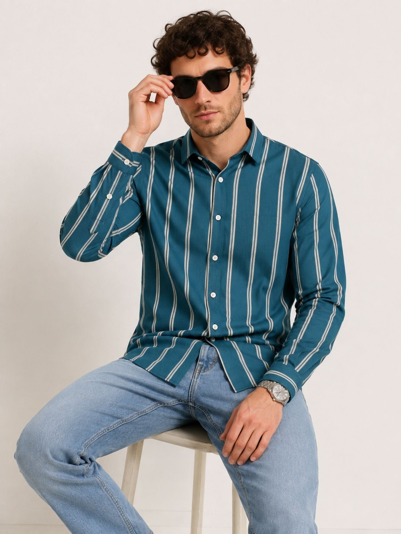 Model seated in Aeron deep teal striped shirt with light blue jeans